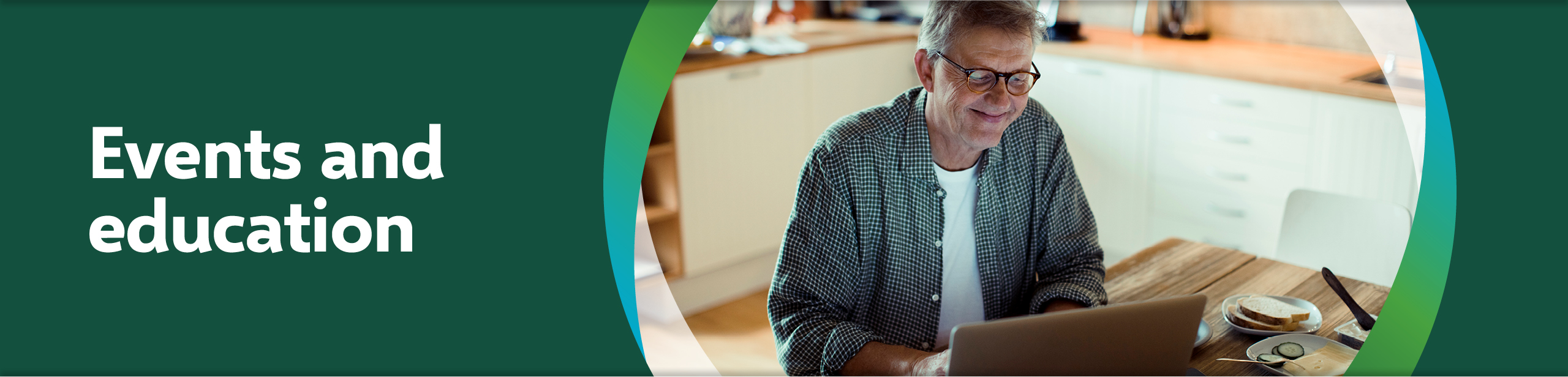 Events and education. Smiling man looking at laptop at kitchen table.